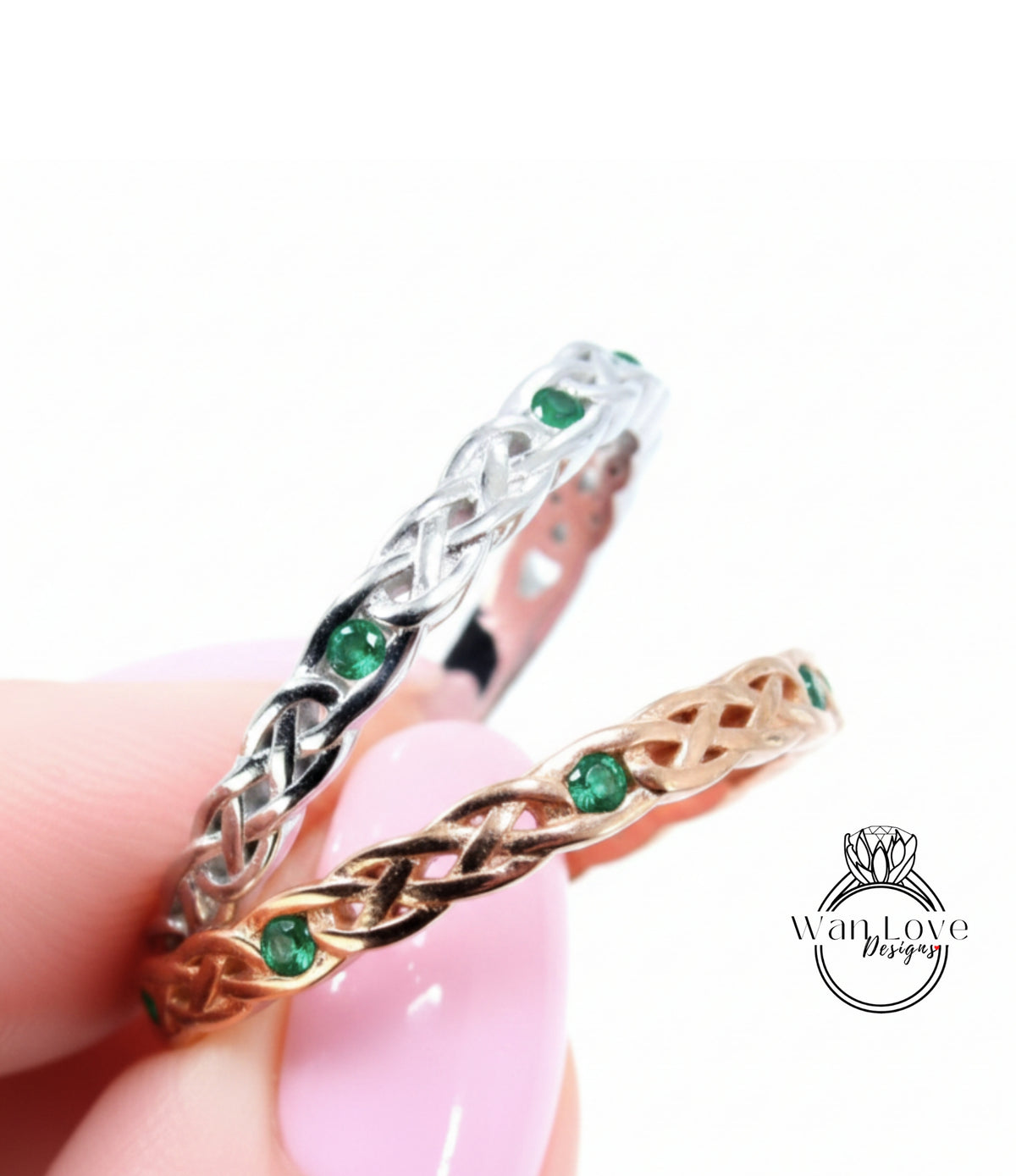 A hand holding two rings with intricate designs and green gemstones.