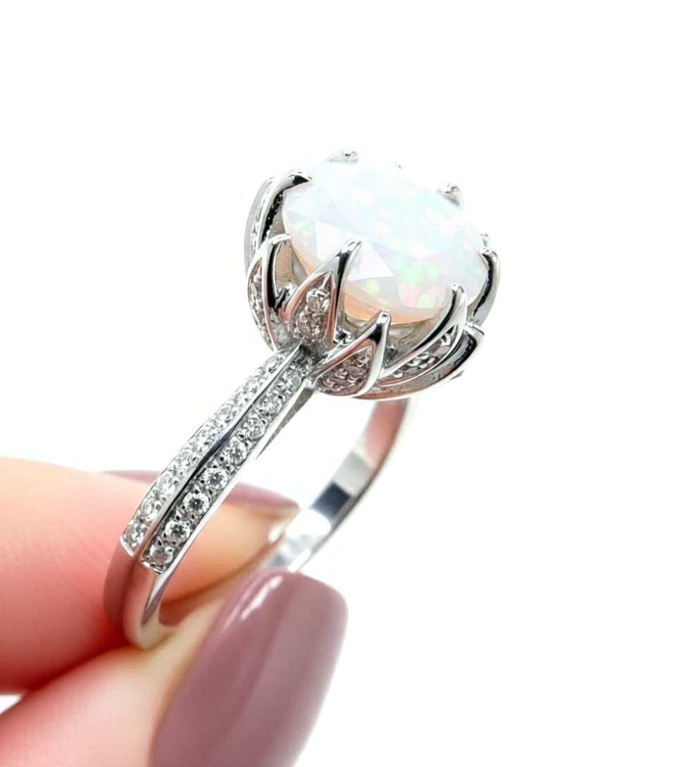 A close-up image of a person's hand holding a silver ring with a large, round opal gemstone.