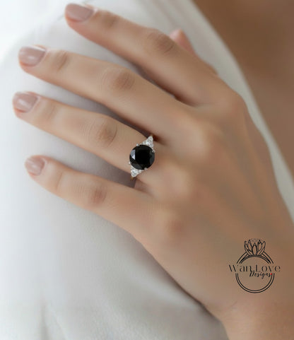 A close-up of a hand wearing a diamond engagement ring with a large black gemstone.