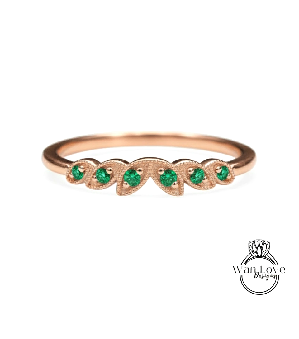 A rose gold ring with a leaf-shaped design and green gemstones.