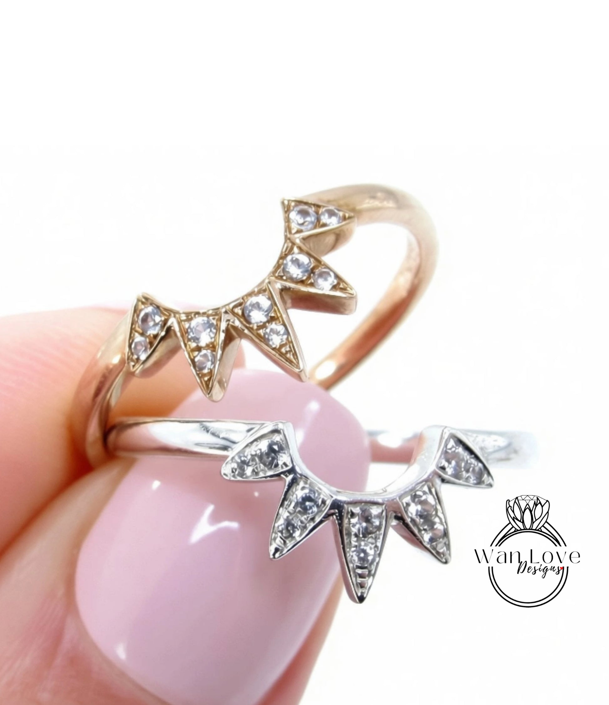 A close-up of a person's hand holding two rings with diamond-encrusted designs.