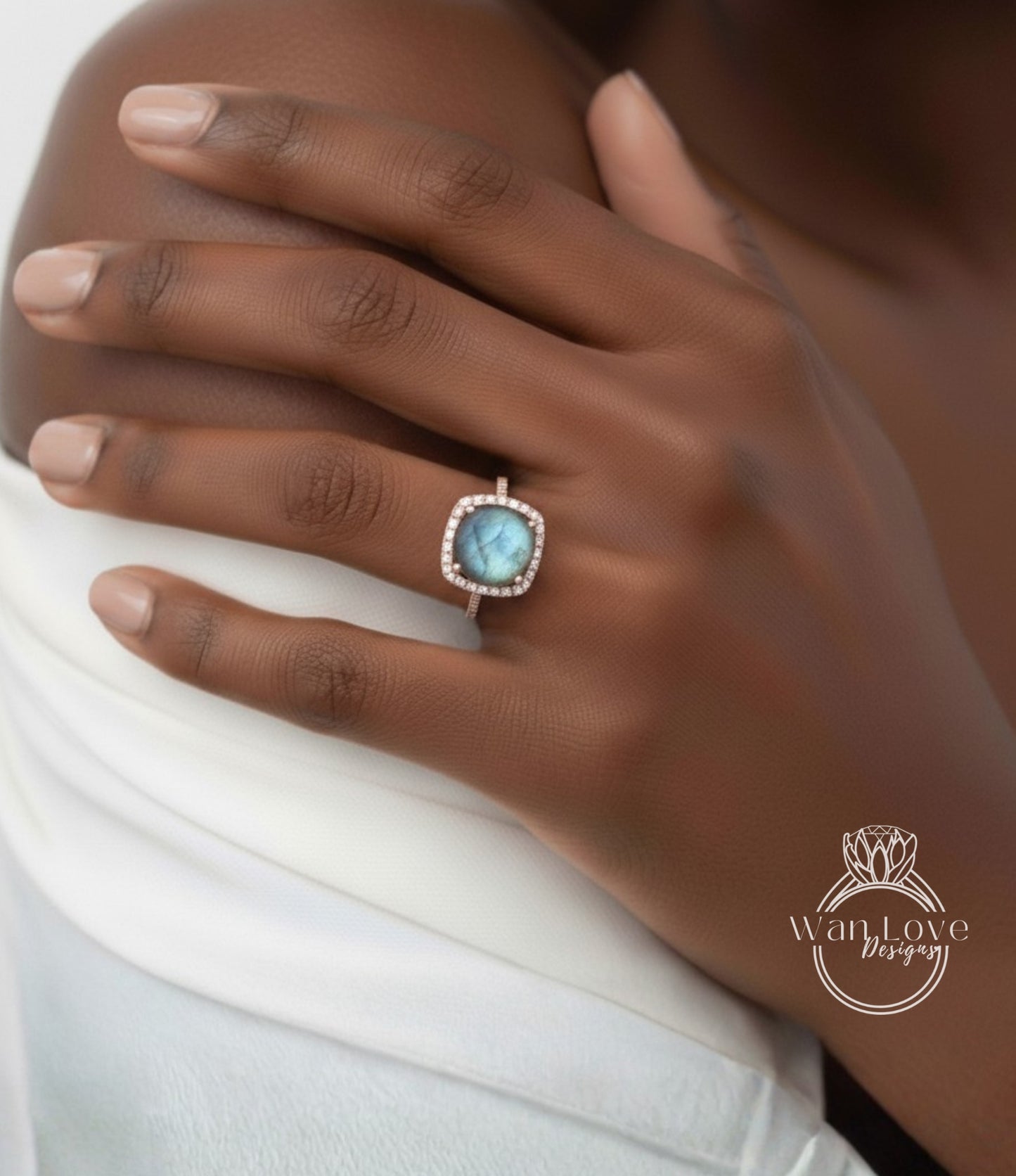 A close-up of a hand wearing a ring with a blue gemstone, resting on a white fabric.