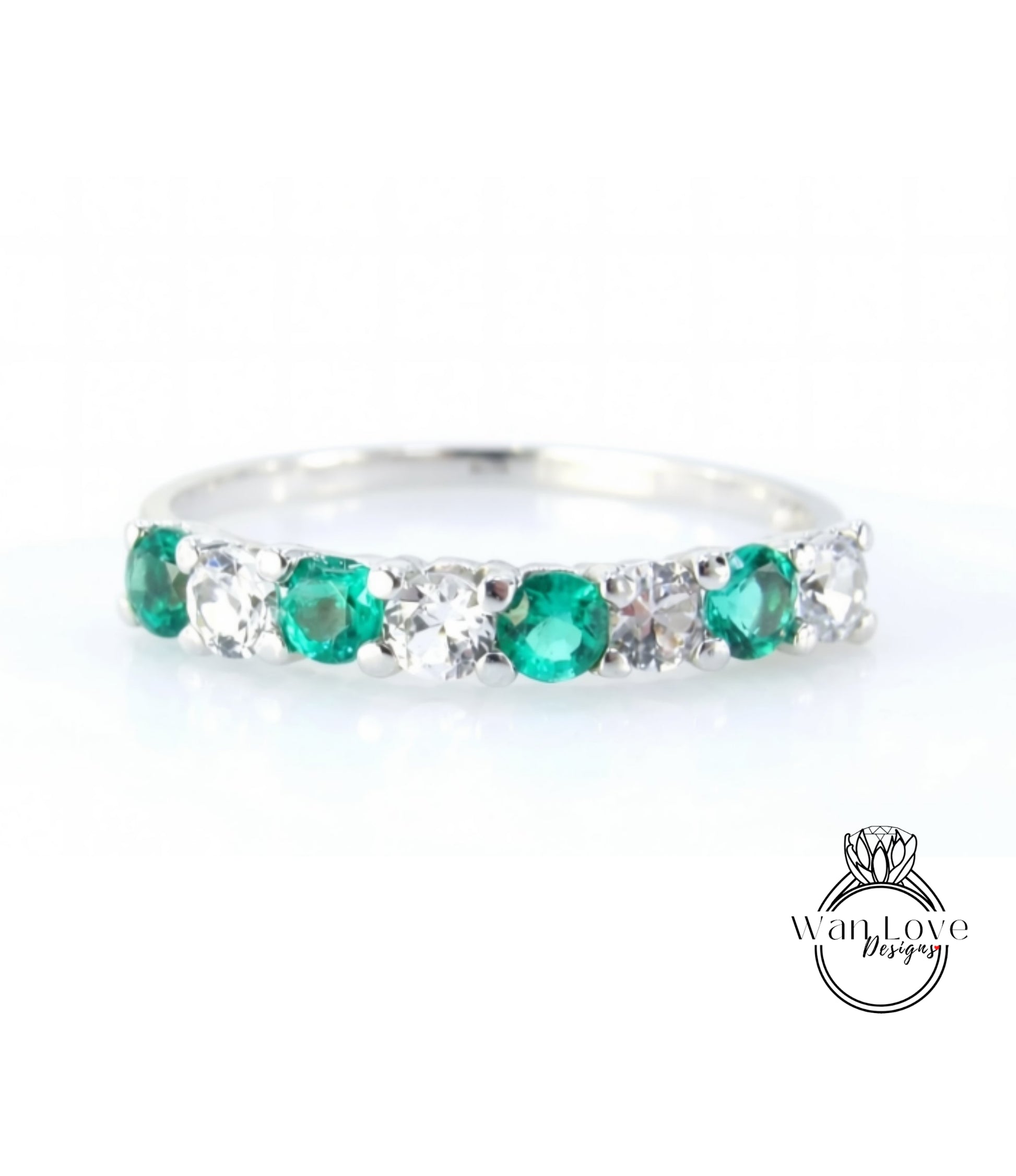 A silver ring with a row of green and white gemstones, including diamonds, set in a band.