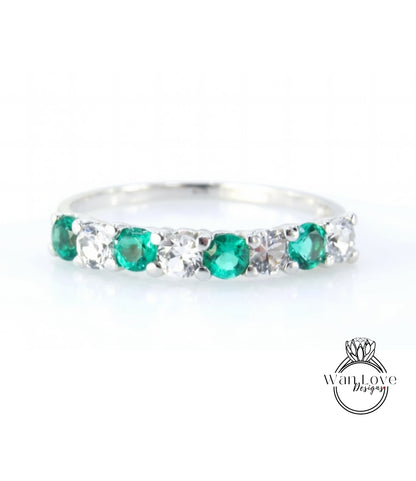 A silver ring with a row of green and white gemstones, including diamonds, set in a band.