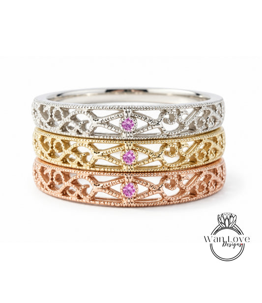 A three-band ring with intricate designs and a central pink gemstone.