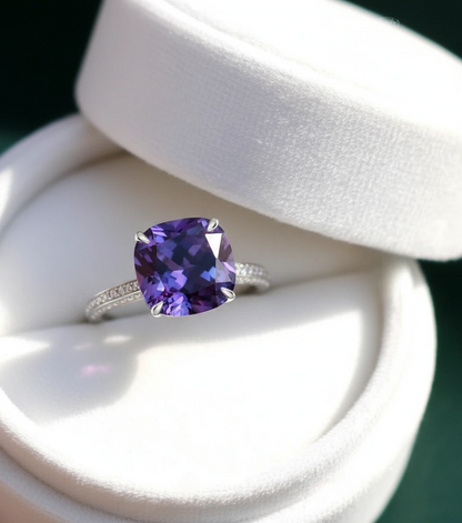 A close-up view of a ring with a large, deep purple gemstone set in a silver band, placed in a white jewelry box.