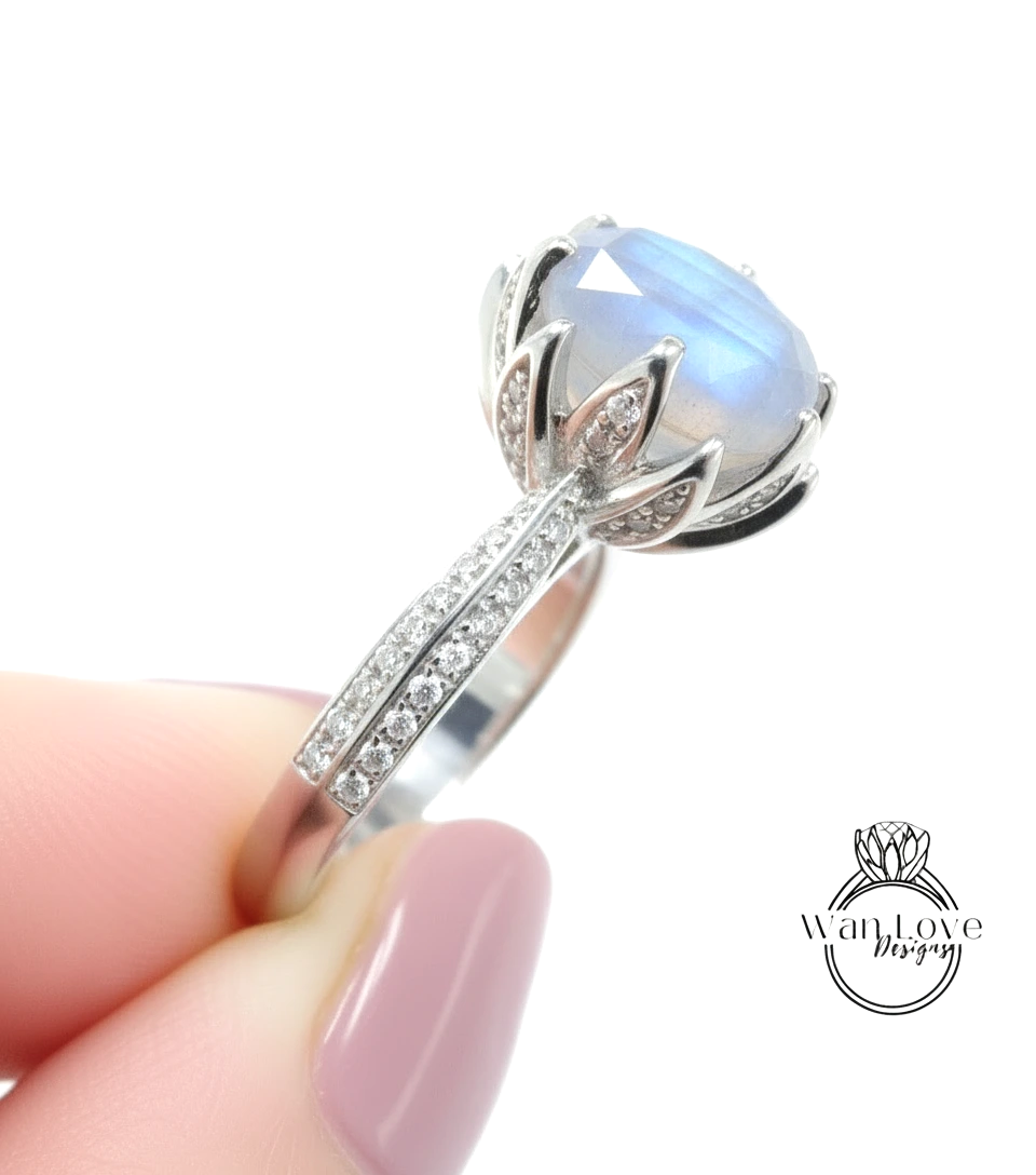 A close-up of a person's hand holding a silver ring with a large blue gemstone, likely a diamond, on the ring.