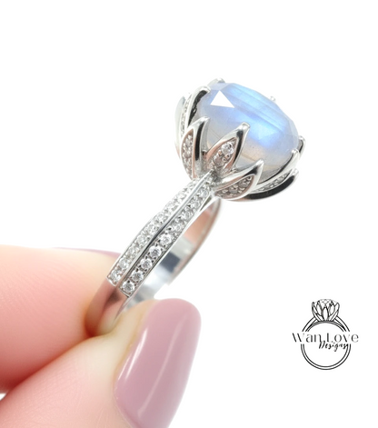 A close-up of a person's hand holding a silver ring with a large blue gemstone, likely a diamond, on the ring.