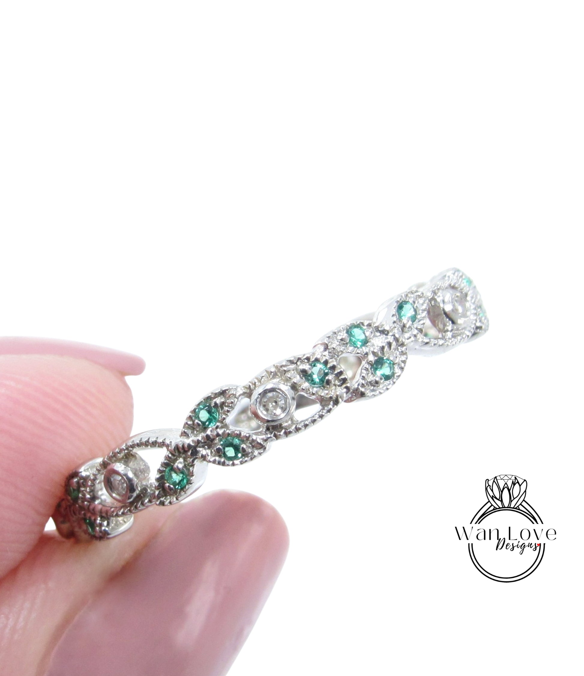 A close-up image of a person's hand holding a silver ring adorned with green gemstones.