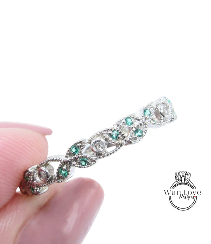 A close-up image of a person's hand holding a silver ring adorned with green gemstones.