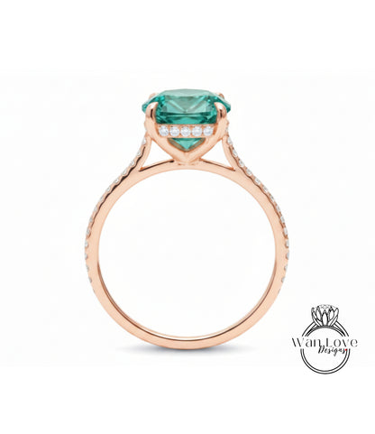 A rose gold engagement ring with a large, round, green gemstone set in the center, surrounded by smaller diamonds.