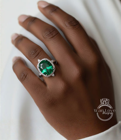 A close-up of a hand wearing a large, oval-shaped green gemstone ring with a halo of smaller diamonds around it.