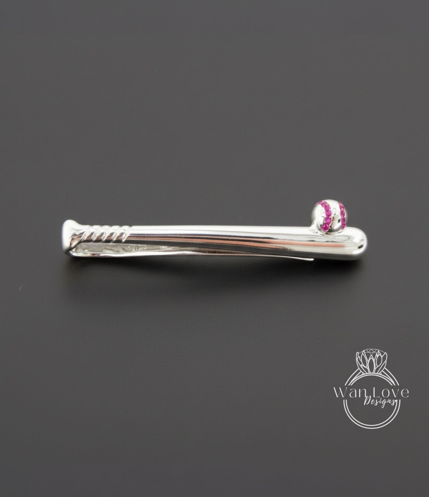 A silver tie clip with a baseball design on it, placed on a black background.