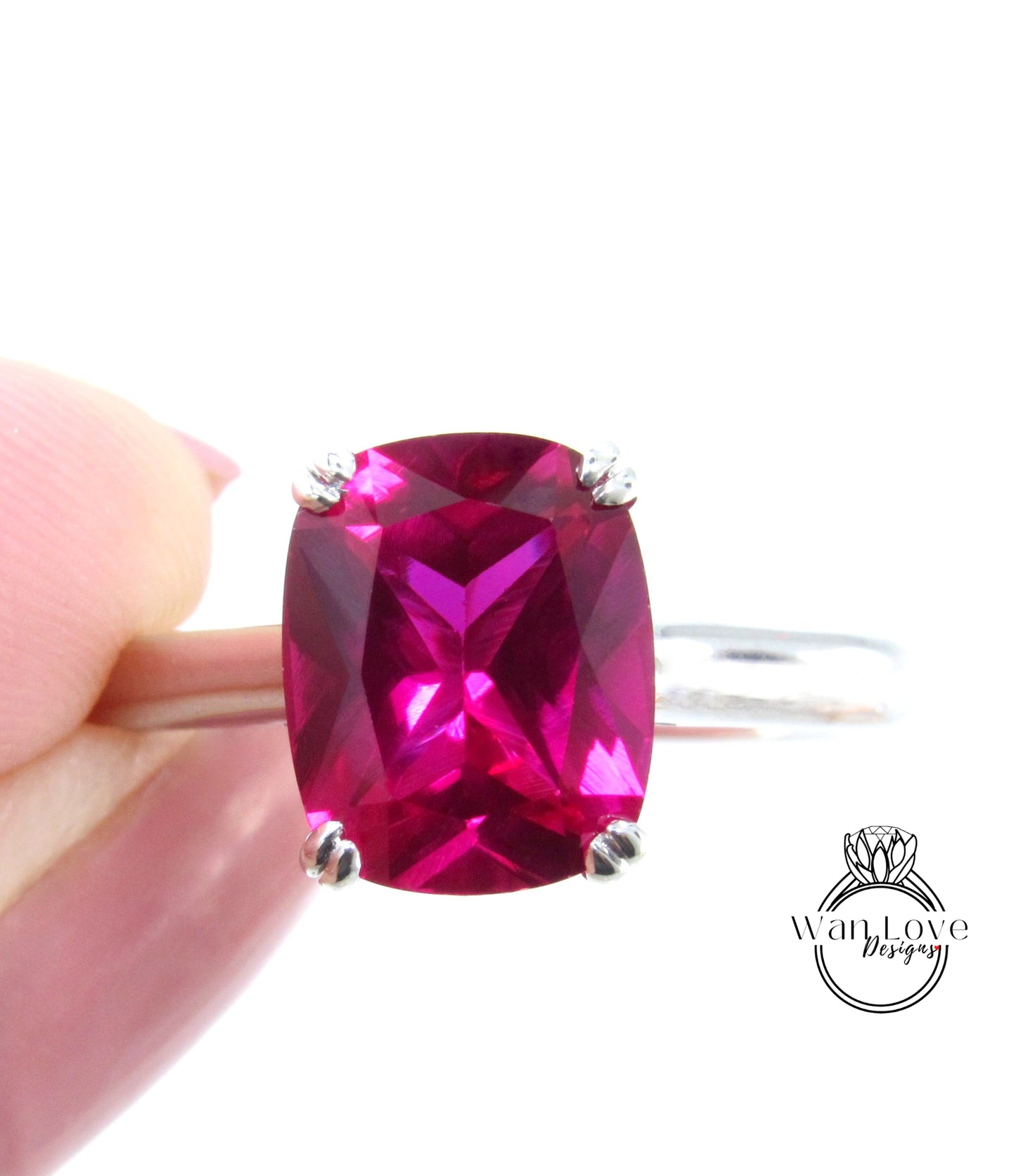A close-up image of a person's hand holding a ring with a large, bright pink gemstone.