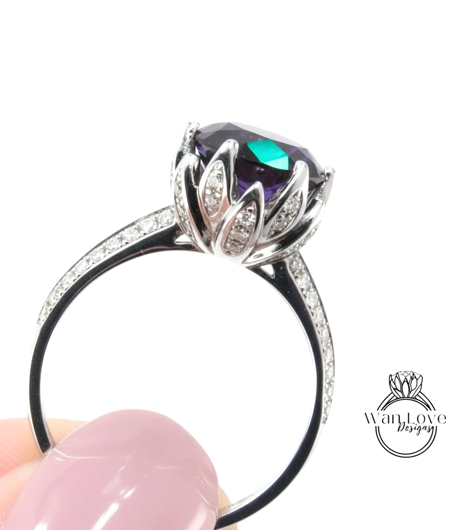 A close-up of a silver ring with a large purple gemstone, held in someone's hand against a white background.