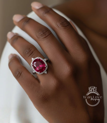 A close-up of a hand wearing a large, red gemstone ring with a halo of smaller diamonds around it.