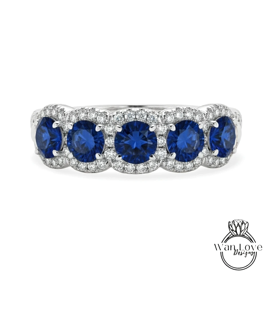 A silver ring with a row of blue sapphire gemstones set in a halo of smaller diamonds.