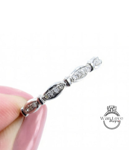 A close-up image of a person's hand holding a silver ring with a row of small diamonds along the band.