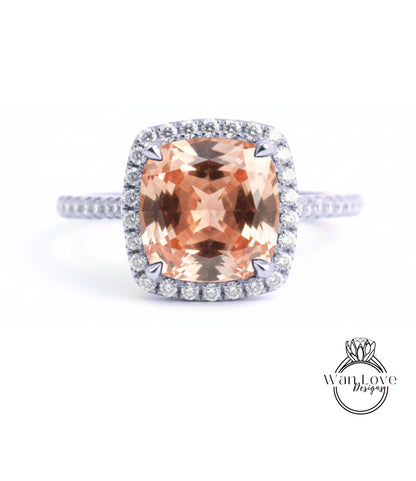 A large, peach-colored gemstone set in a halo of smaller diamonds, with a silver band around the base.