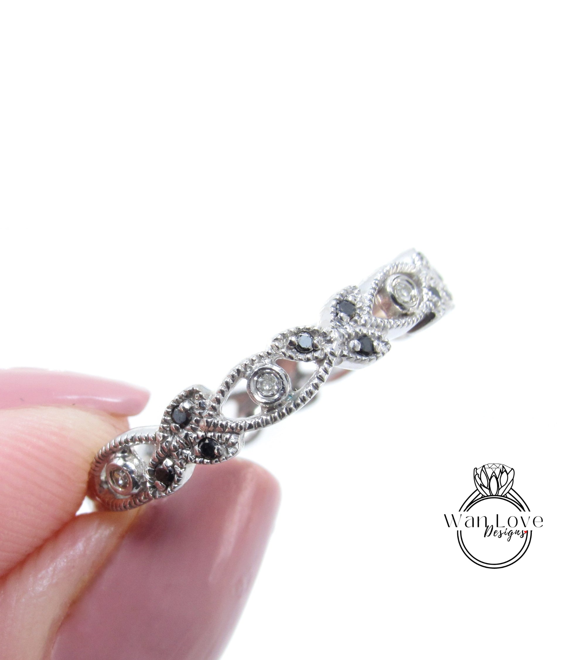A close-up image of a person's hand holding a silver ring adorned with black gemstones.