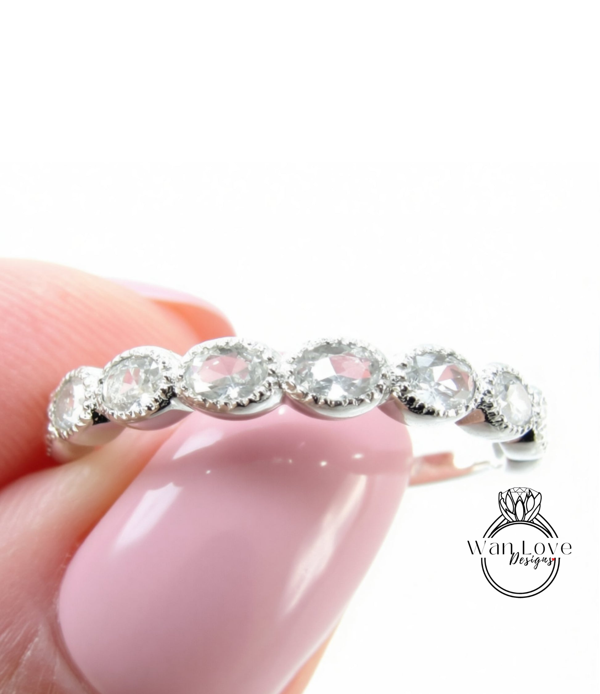A close-up of a person's hand holding a ring with a row of clear gemstones on it.