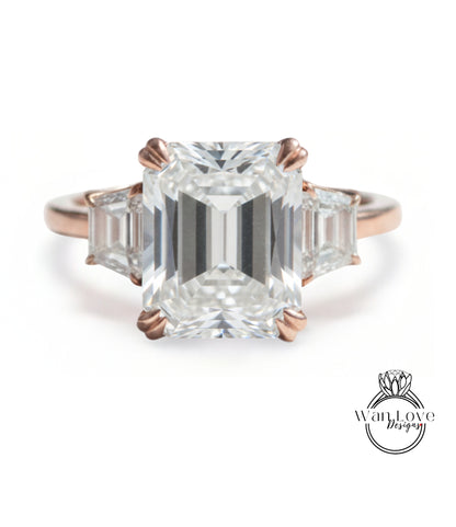 A large, clear gemstone engagement ring with a prominent central diamond surrounded by smaller diamonds on either side.