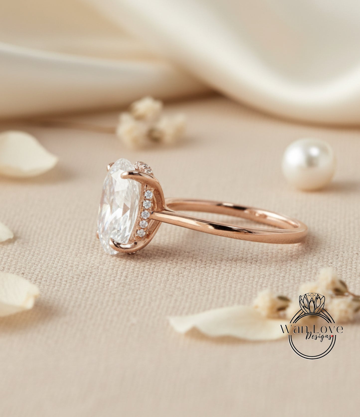 A rose gold engagement ring with a large oval-shaped diamond and a halo of smaller diamonds around the center stone, placed on a beige fabric surface with scattered white flower petals.