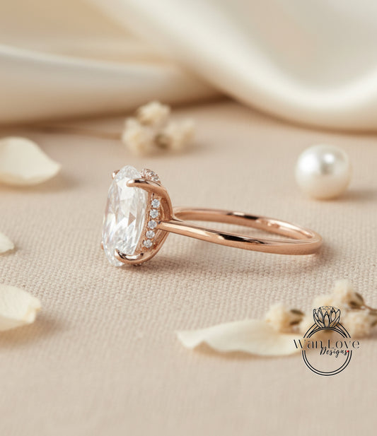 A rose gold engagement ring with a large oval-shaped diamond and a halo of smaller diamonds around the center stone, placed on a beige fabric surface with scattered white flower petals.