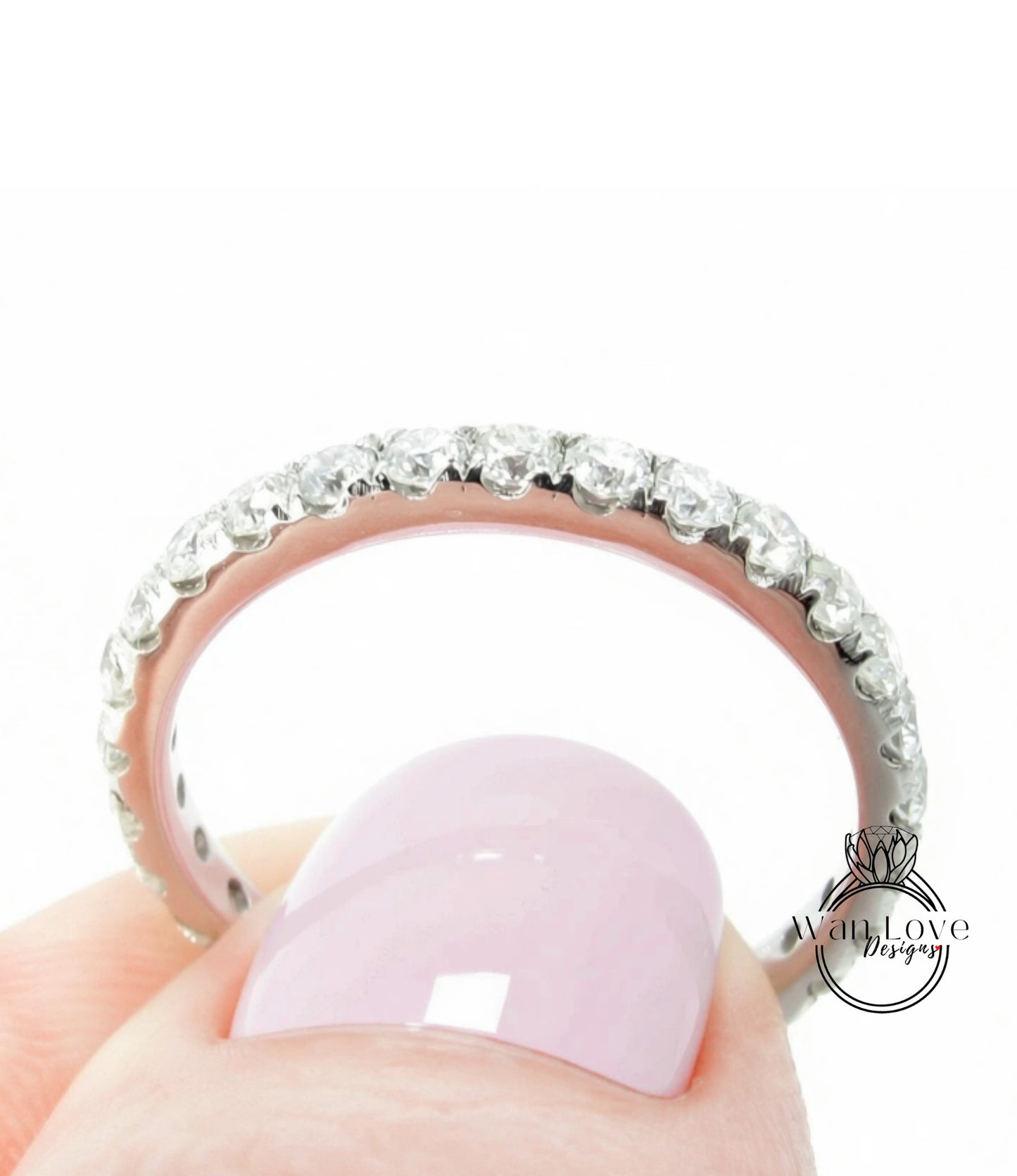 A close-up of a person's hand holding a ring with a row of diamonds on the band.