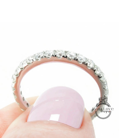 A close-up of a person's hand holding a ring with a row of diamonds on the band.