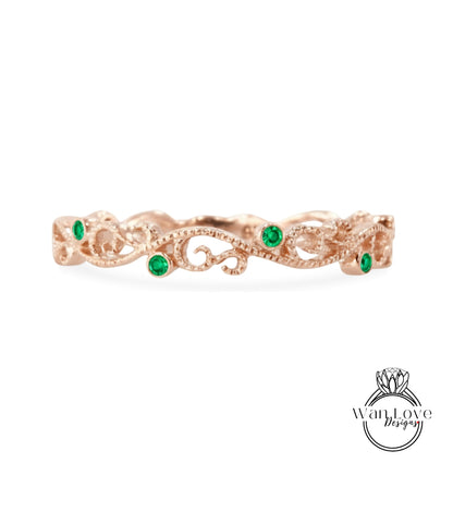 A rose gold ring with a decorative floral design and green gemstones.