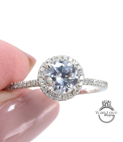 A close-up image of a person's hand holding a diamond engagement ring with a large central diamond surrounded by smaller diamonds on the band.