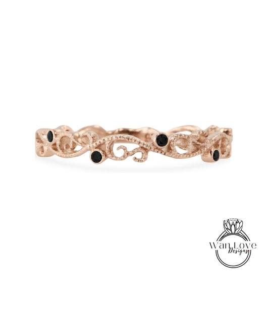 A rose gold ring with a decorative scroll design and small black gemstones.
