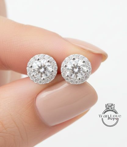 A close-up of a person's hand holding a pair of diamond earrings with a large central diamond surrounded by smaller diamonds.