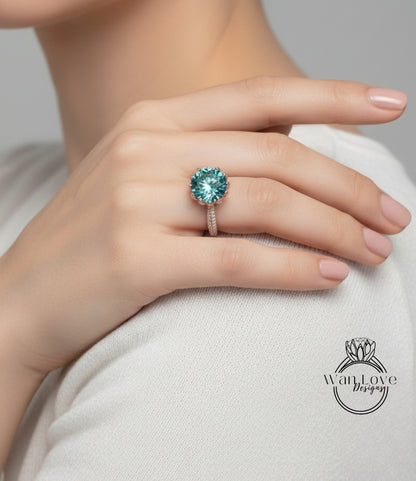 A close-up of a person's hand wearing a large, turquoise-colored diamond ring on the ring finger.