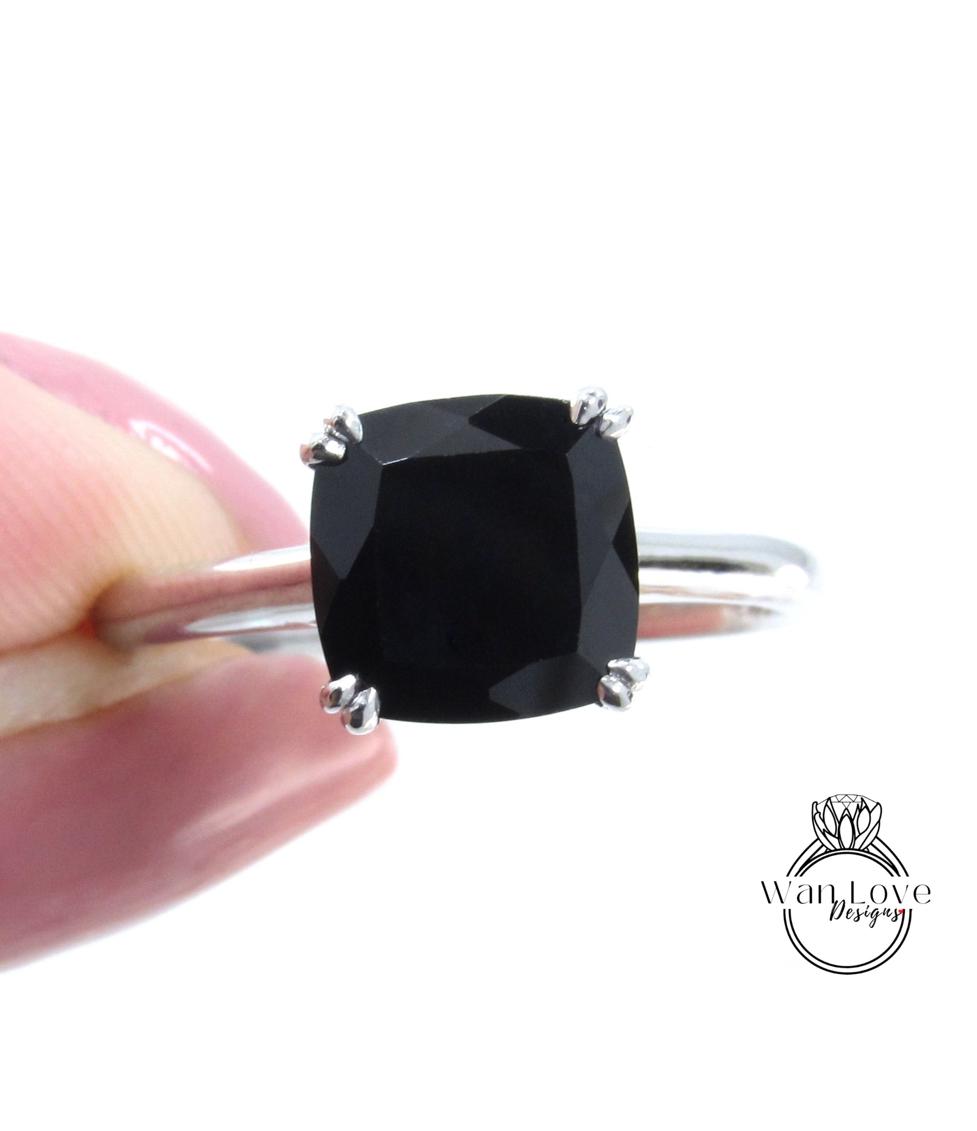 A close-up image of a person's hand holding a silver ring with a large black gemstone, likely a diamond.