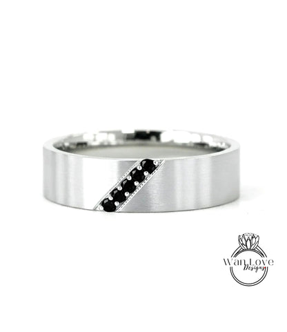 A silver-colored ring with a diagonal line through it, featuring small black stones or diamonds.