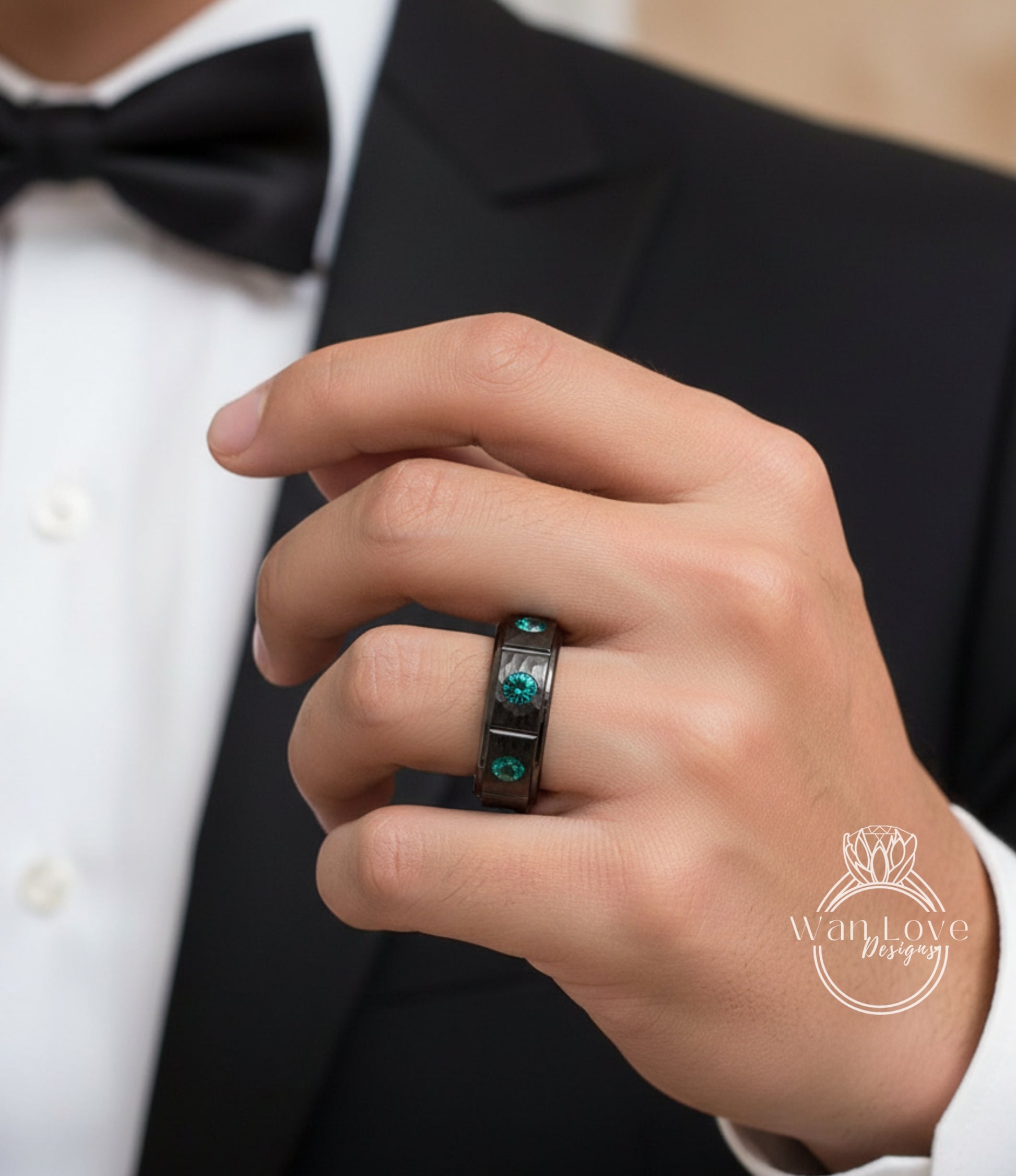A close-up of a person's hand wearing a ring with green gemstones, wearing a black suit jacket.