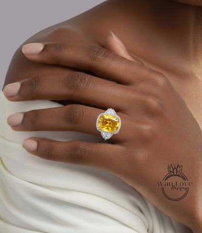 A close-up of a person's hand wearing a large, yellow gemstone ring with a diamond accent.