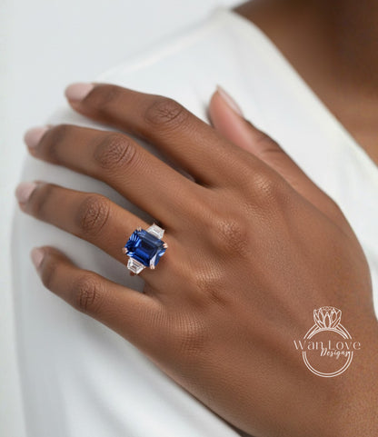 A close-up of a hand wearing a ring with a large blue gemstone, likely a sapphire, on the ring finger.