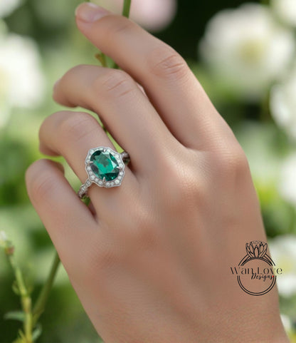 A close-up of a hand wearing a ring with a large oval-shaped gemstone, likely an emerald, set in a halo of smaller diamonds.