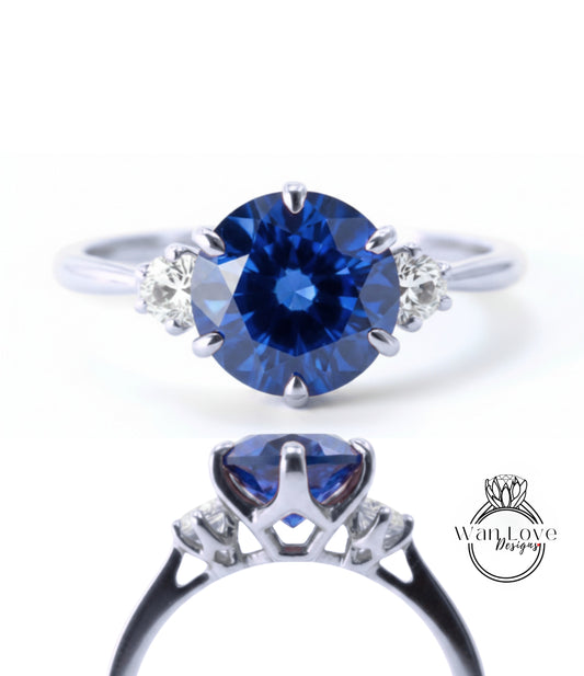 a silver ring with a large blue gemstone, likely a sapphire, as the centerpiece. The ring is adorned with smaller diamonds on either side of the blue gemstone, creating a striking contrast against the silver band.