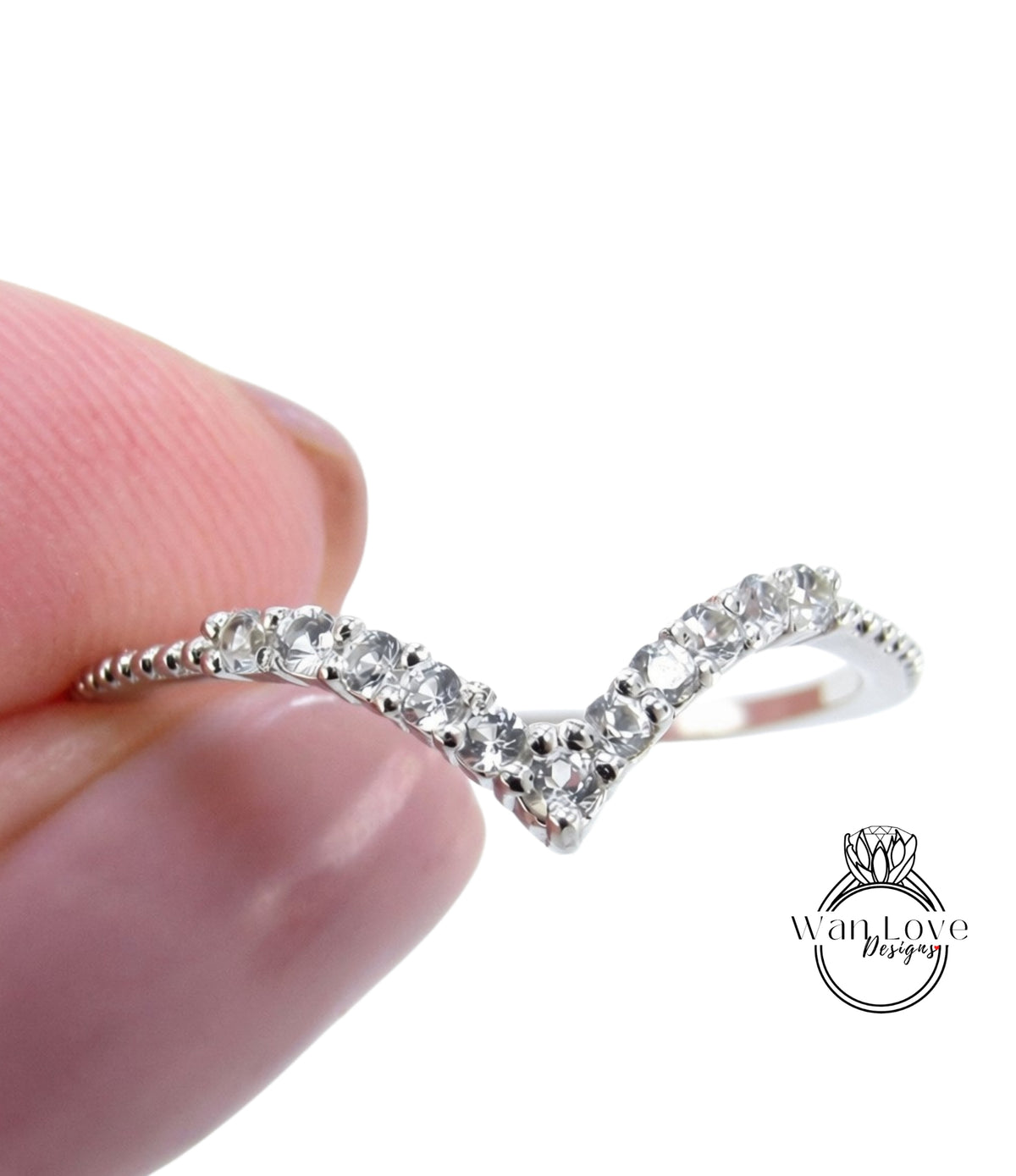 A close-up image of a person's hand holding a silver ring with a v-shaped design and small clear gemstones.