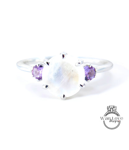 A silver ring with a large moonstone and two purple gemstones on either side.
