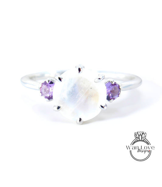 A silver ring with a large moonstone and two purple gemstones on either side.