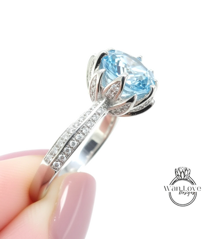 A close-up of a person's hand holding a silver ring with a large blue gemstone, likely an aquamarine or light blue gemstone.