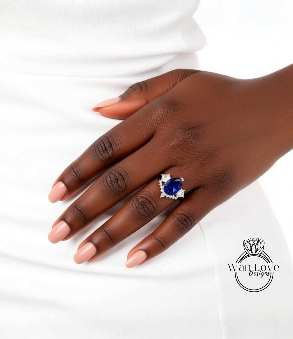 A close-up of a hand wearing a ring with a blue gemstone, resting on a white dress.