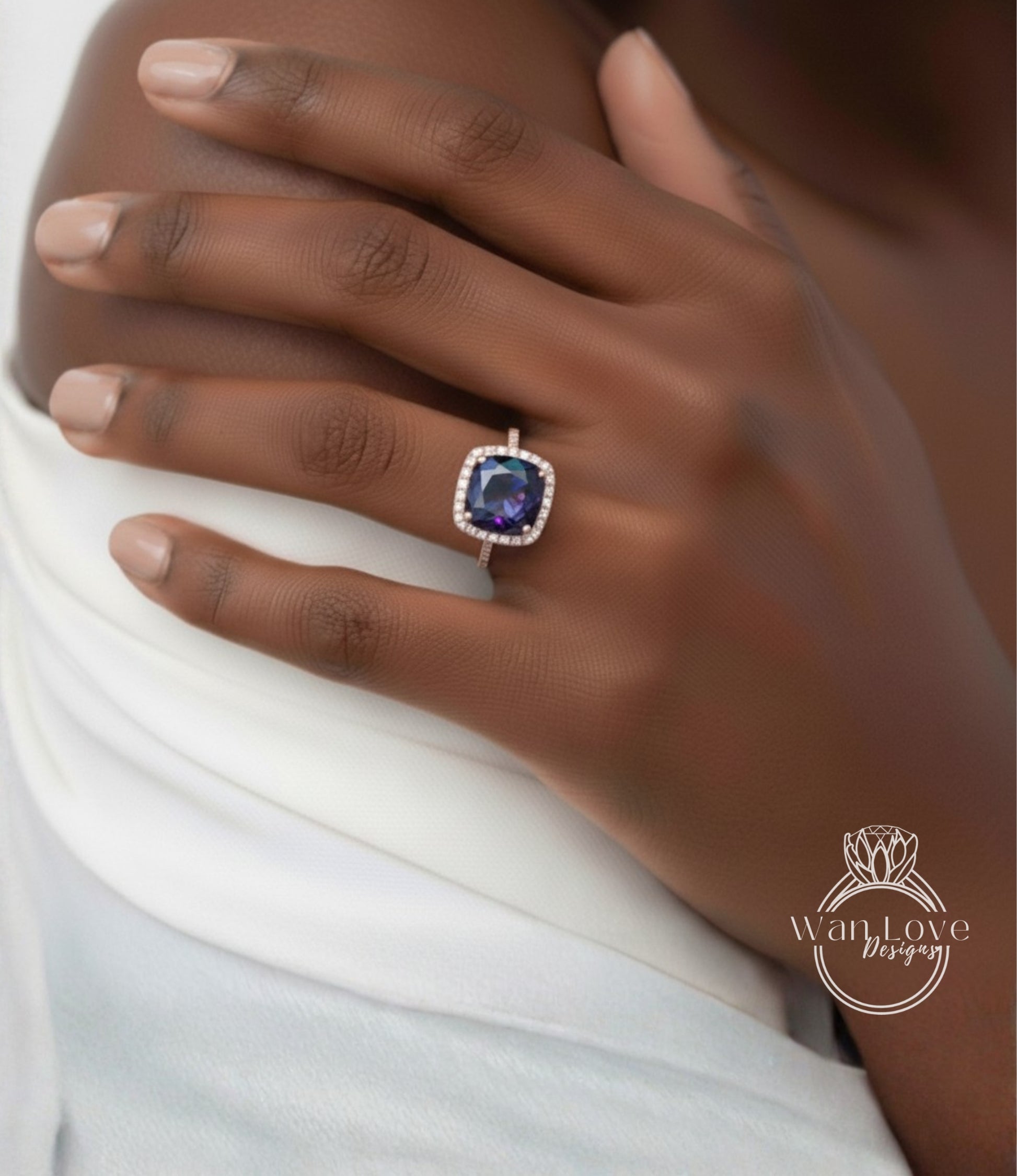 A close-up of a hand wearing a ring with a large blue gemstone, resting on a white fabric.
