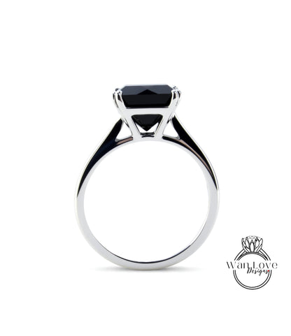 A silver ring with a large black gemstone, likely a diamond, set in the center.