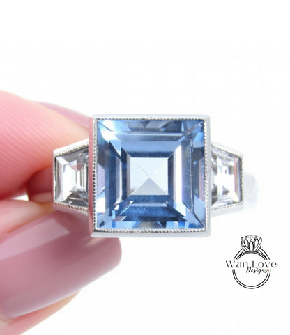 A close-up image of a person's hand holding a ring with a large blue gemstone, likely a diamond.